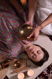 Woman undergoing singing bowl therapy indoors, top view