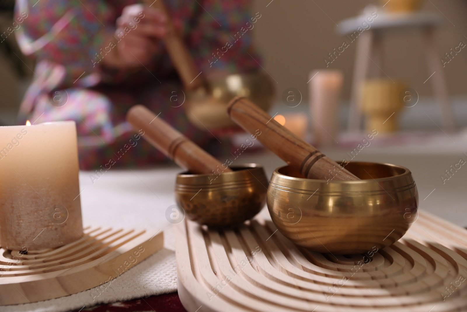 Photo of Woman with singing bowls and burning candles indoors, selective focus