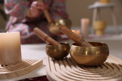 Photo of Woman with singing bowls and burning candles indoors, selective focus