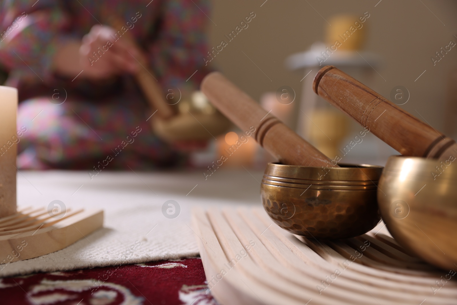 Photo of Woman with singing bowls and burning candles indoors, selective focus