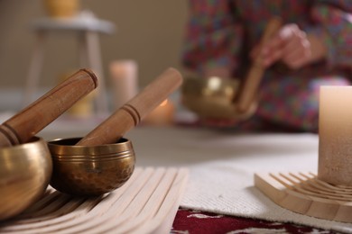 Photo of Woman with singing bowls and burning candles indoors, selective focus