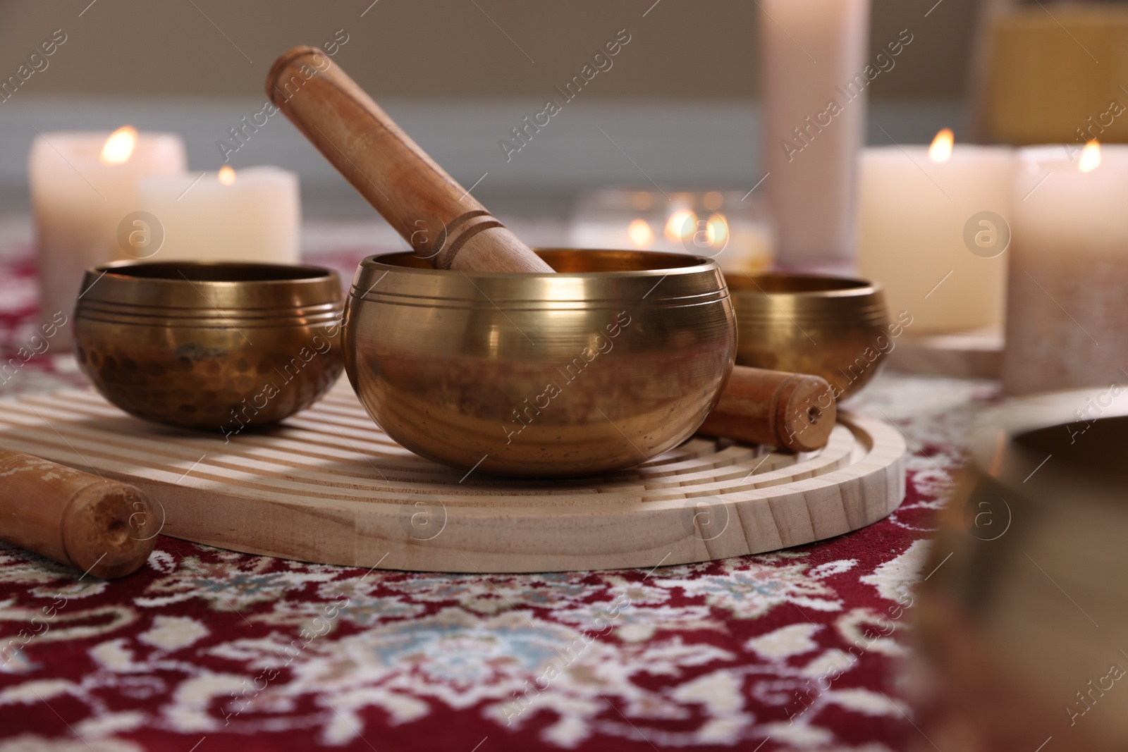 Photo of Singing bowls with mallet and burning candles on floor indoors, closeup