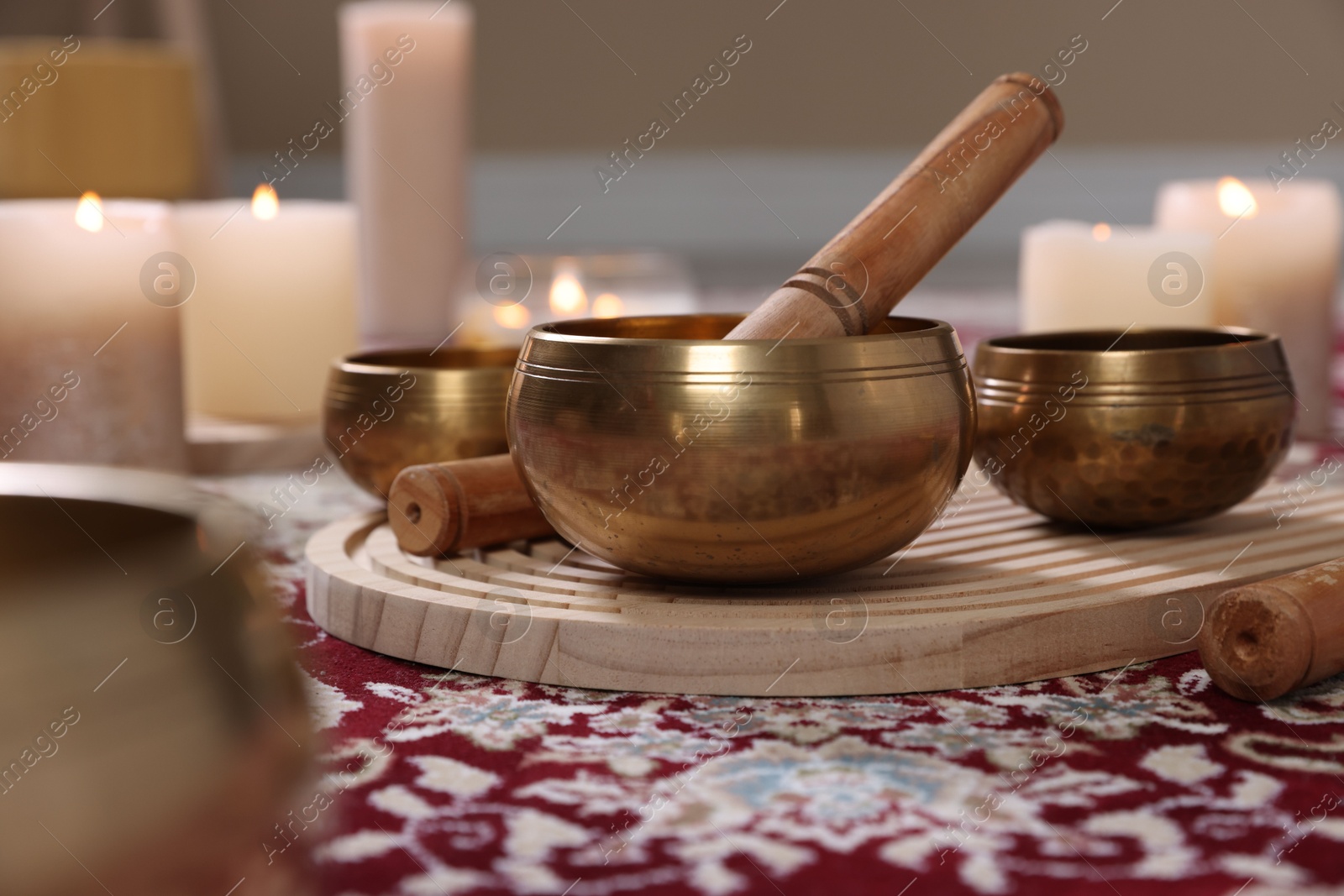 Photo of Singing bowls with mallet and burning candles on floor indoors, closeup