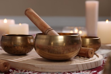 Photo of Singing bowls with mallet and burning candles on floor indoors, closeup