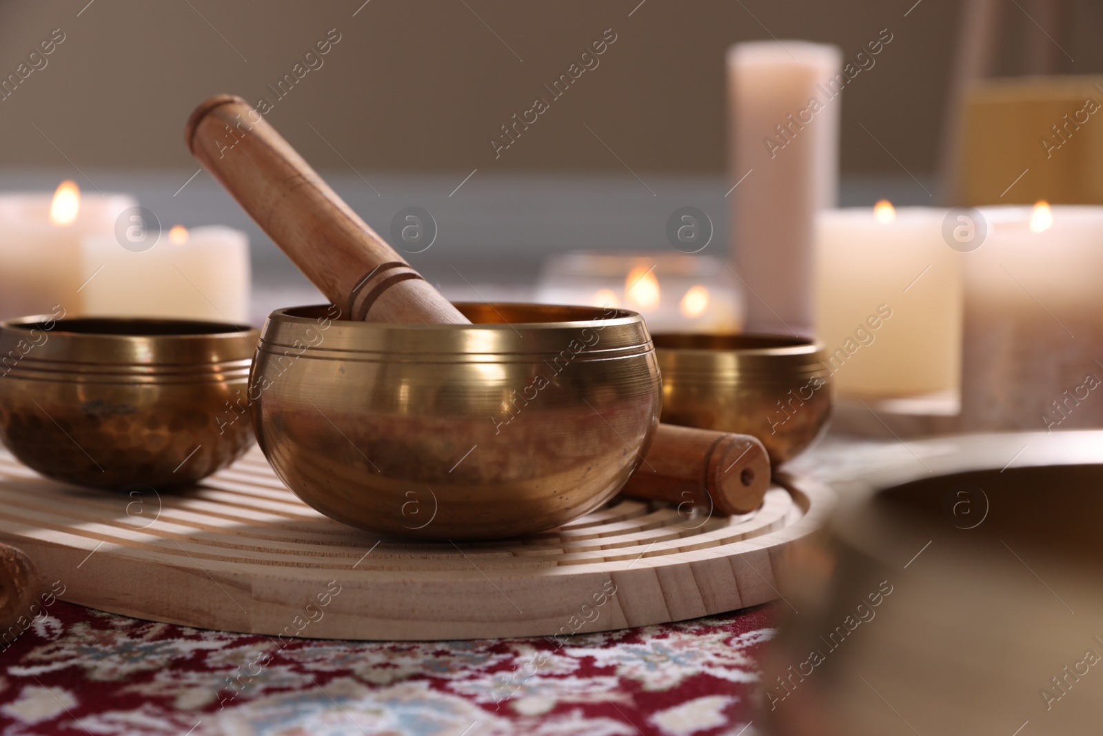 Photo of Singing bowls with mallet and burning candles on floor indoors, closeup