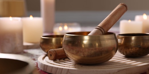 Photo of Singing bowls with mallet and burning candles on floor indoors, closeup