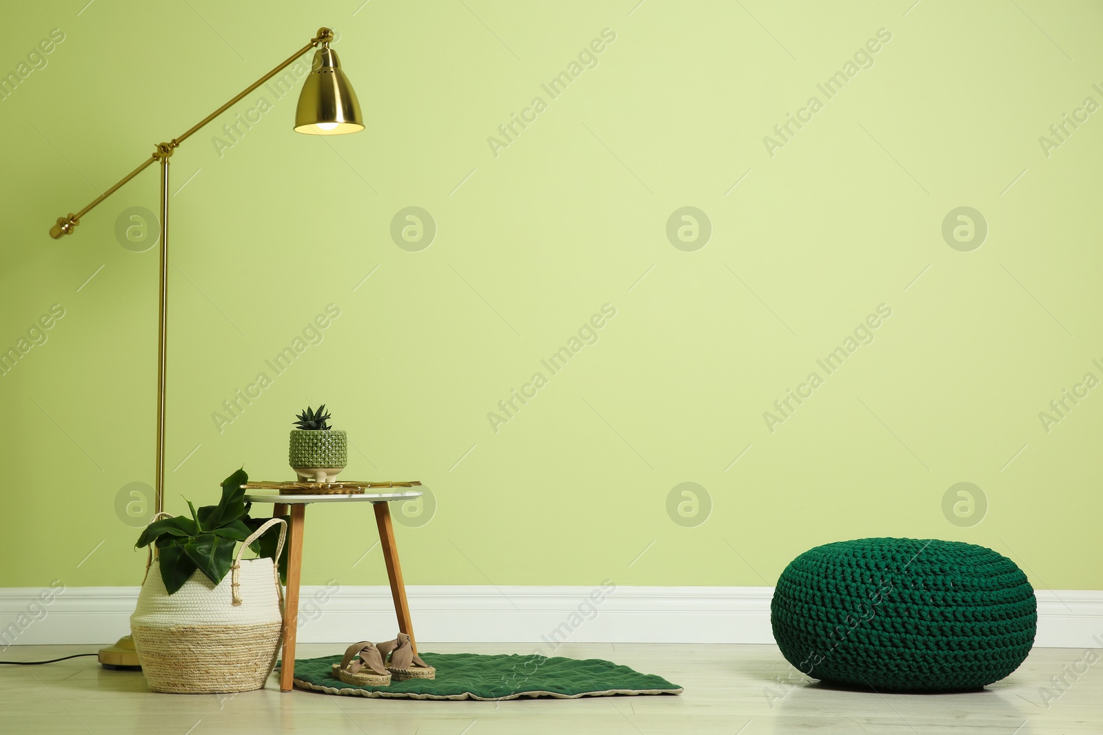 Photo of Stylish room interior with comfortable knitted pouf and plants near light green wall