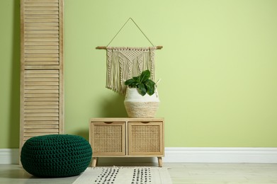 Photo of Stylish room interior with comfortable knitted pouf, wooden furniture and plant near light green wall