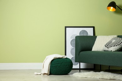 Photo of Stylish living room interior with comfortable knitted pouf and sofa near light green wall, space for text