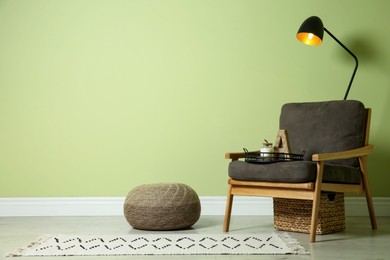 Photo of Stylish room interior with comfortable knitted pouf and armchair near light green wall