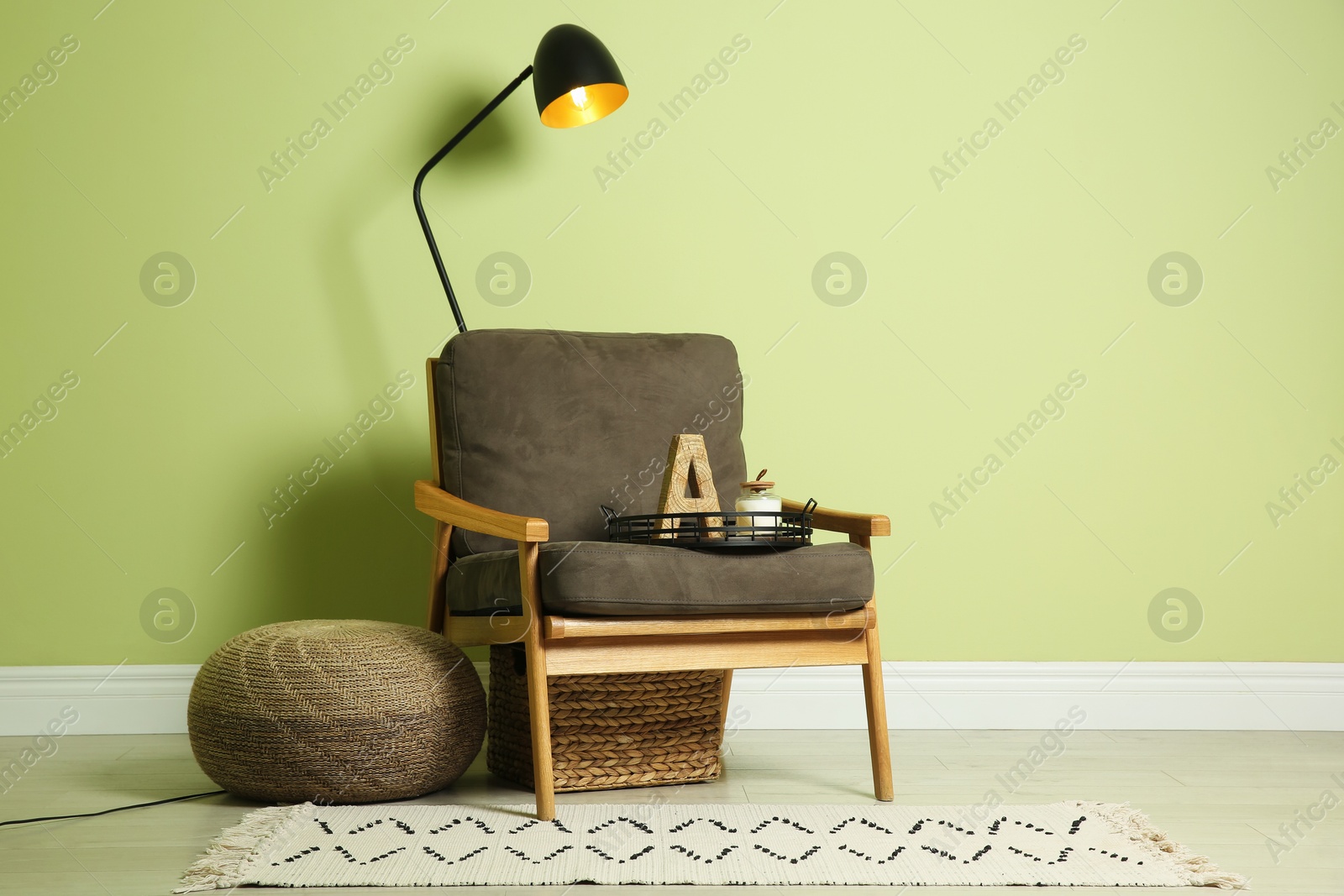 Photo of Stylish room interior with comfortable knitted pouf and armchair near light green wall