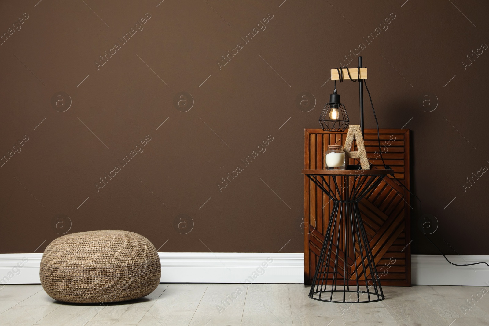 Photo of Comfortable knitted pouf and table with decor elements near brown wall indoors, space for text. Interior design