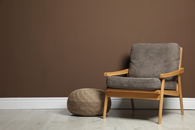 Photo of Stylish knitted pouf and comfortable armchair near brown wall indoors, space for text. Interior design