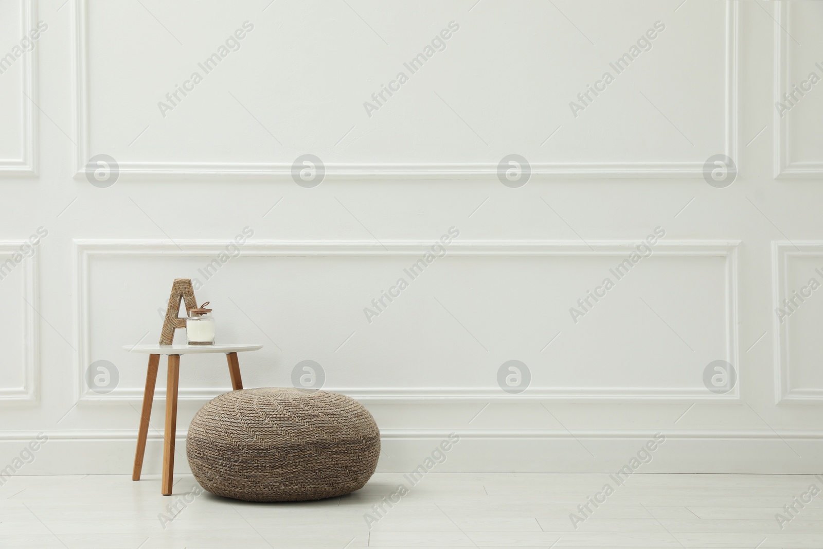 Photo of Knitted pouf and table with decor elements near white wall indoors. Space for text