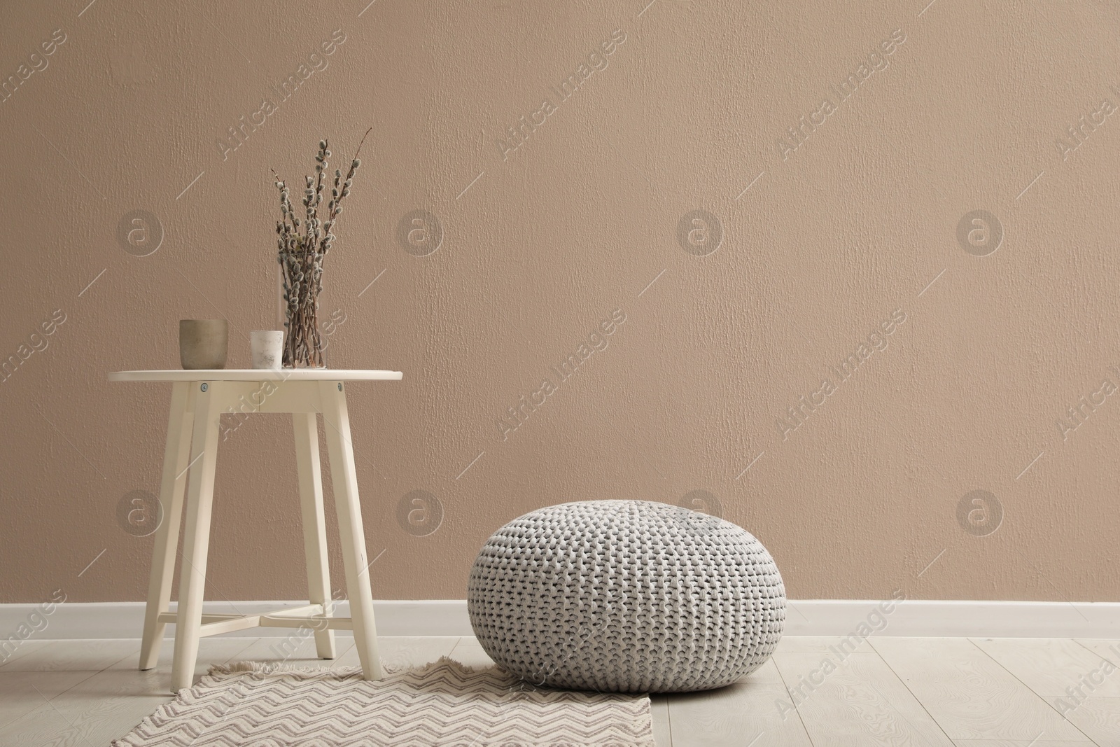 Photo of Knitted pouf and decor elements near beige wall indoors. Space for text