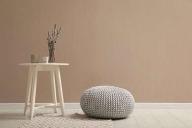 Photo of Knitted pouf and decor elements near beige wall indoors. Space for text