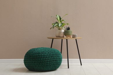 Photo of Knitted pouf and table with houseplants near beige wall indoors. Space for text