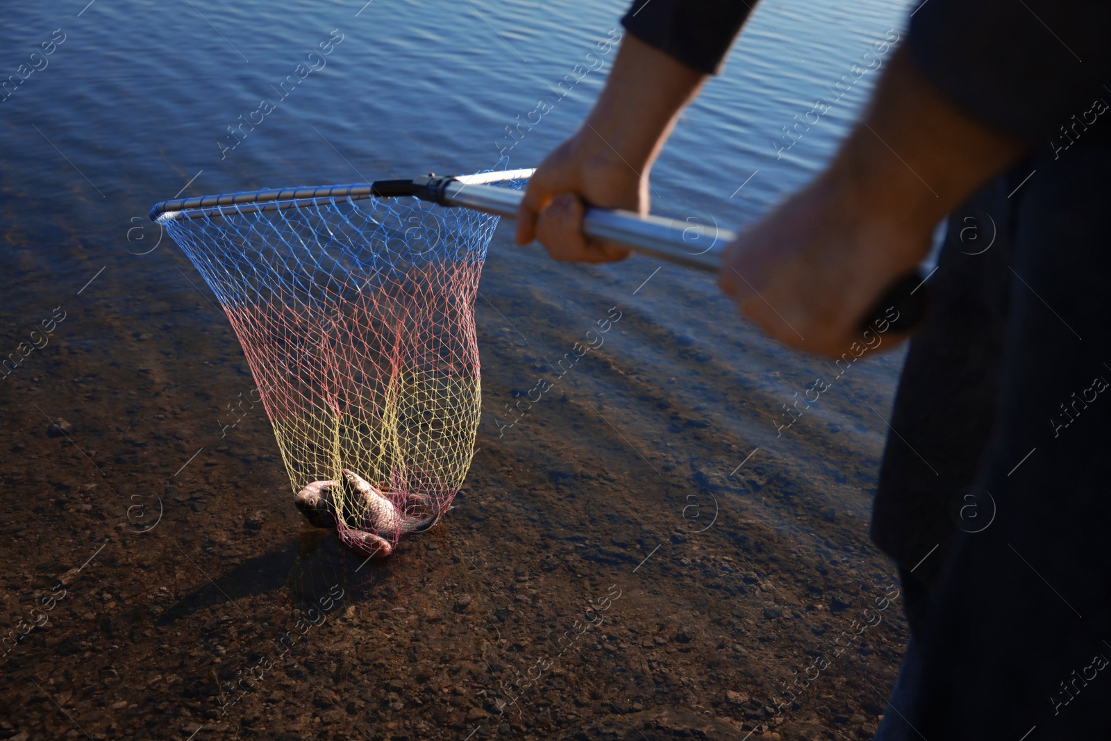 Photo of Fisherman holding fishing net with catch at riverside, closeup