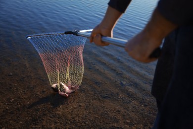 Photo of Fisherman holding fishing net with catch at riverside, closeup