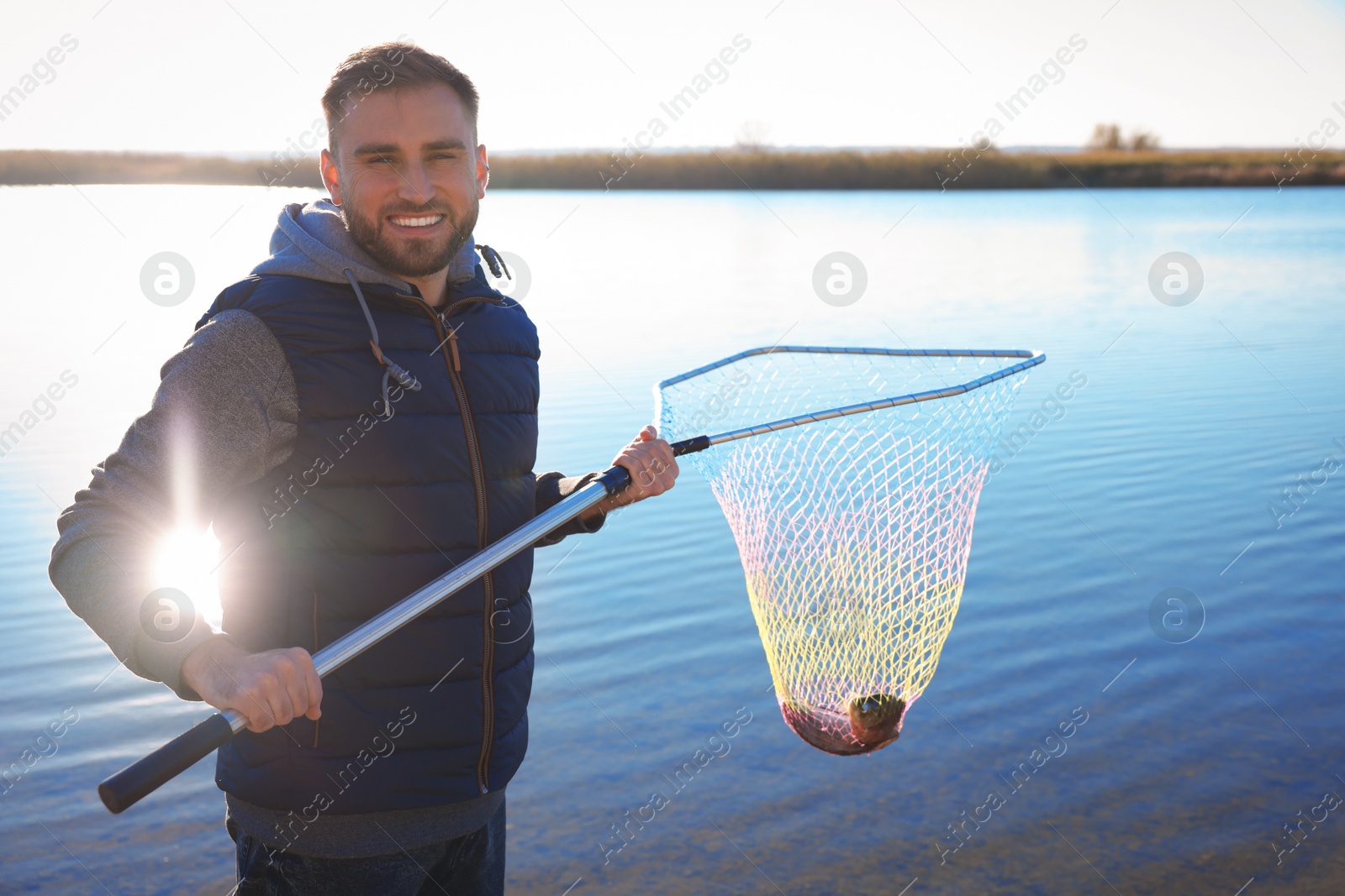 Photo of Fisherman holding fishing net with catch at riverside