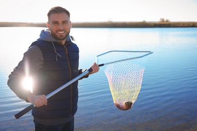 Photo of Fisherman holding fishing net with catch at riverside