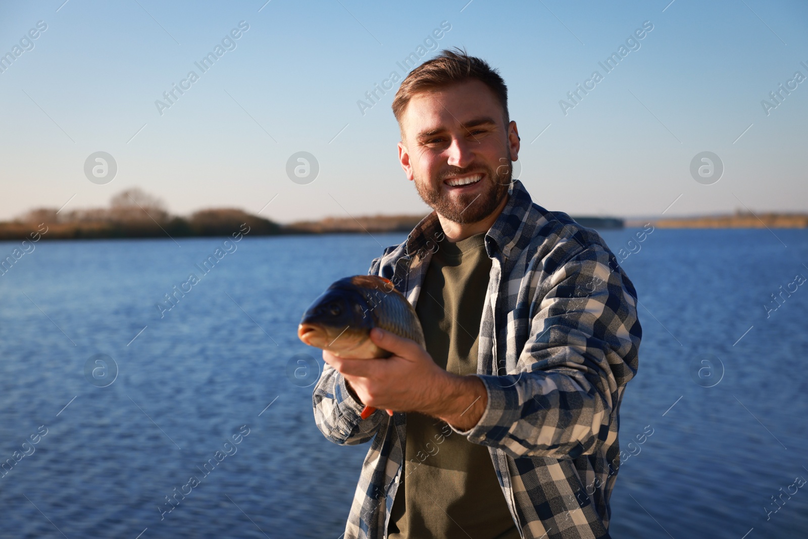 Photo of Fisherman holding caught fish at riverside. Recreational activity