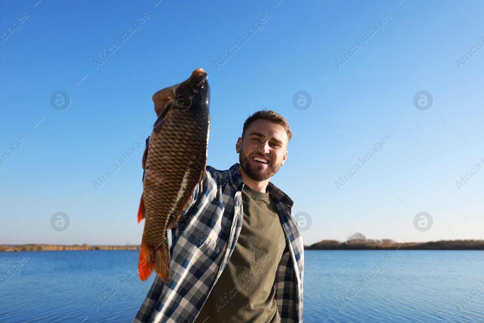 Photo of Fisherman holding caught fish at riverside. Recreational activity