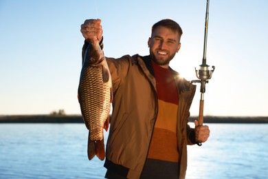 Photo of Fisherman holding rod and catch at riverside, focus on fish