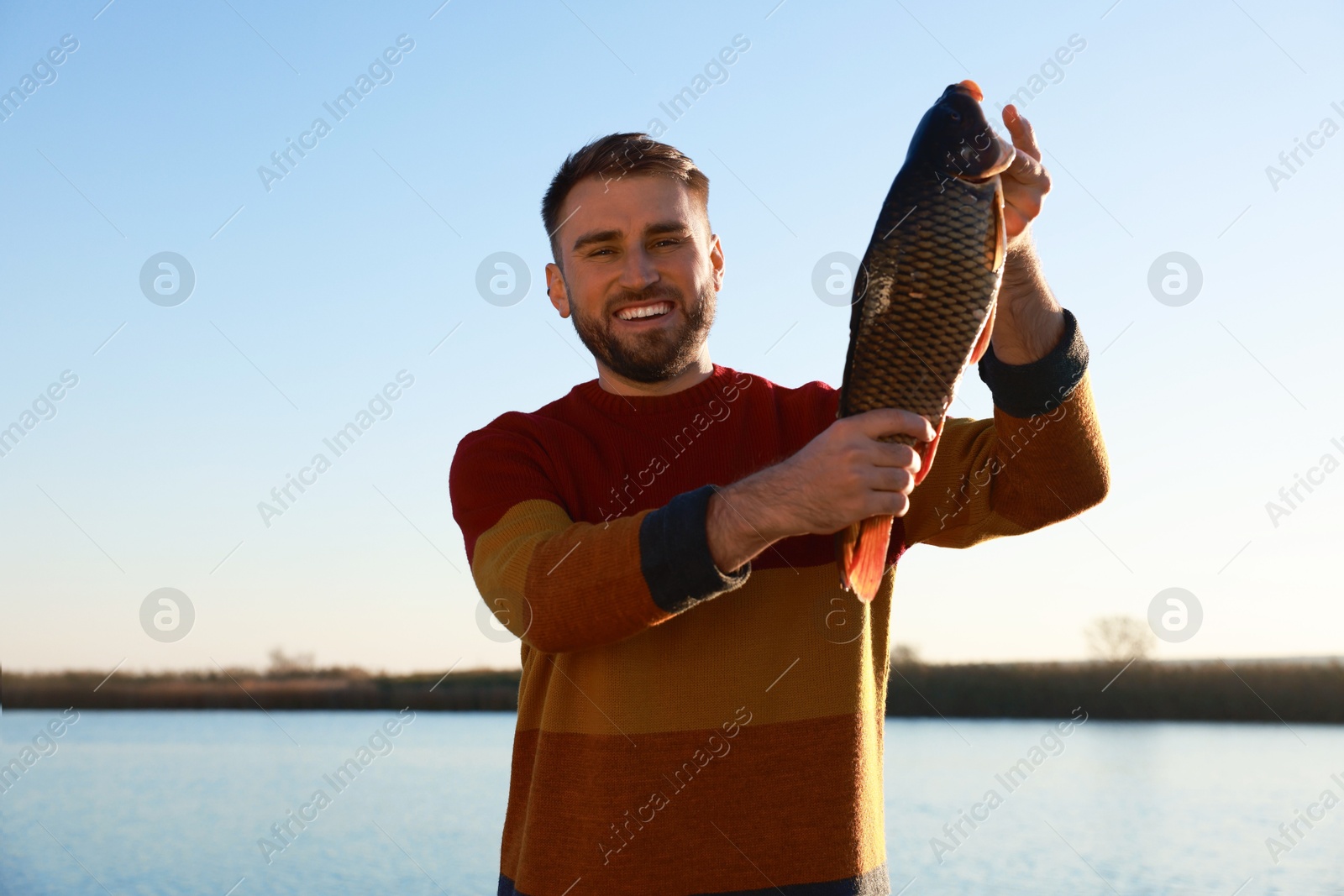 Photo of Fisherman holding caught fish at riverside. Recreational activity