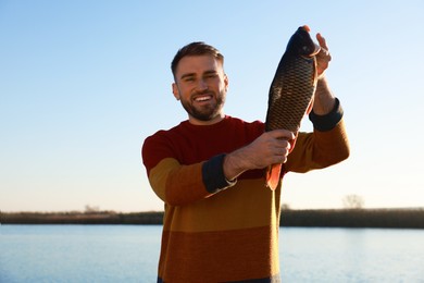 Photo of Fisherman holding caught fish at riverside. Recreational activity