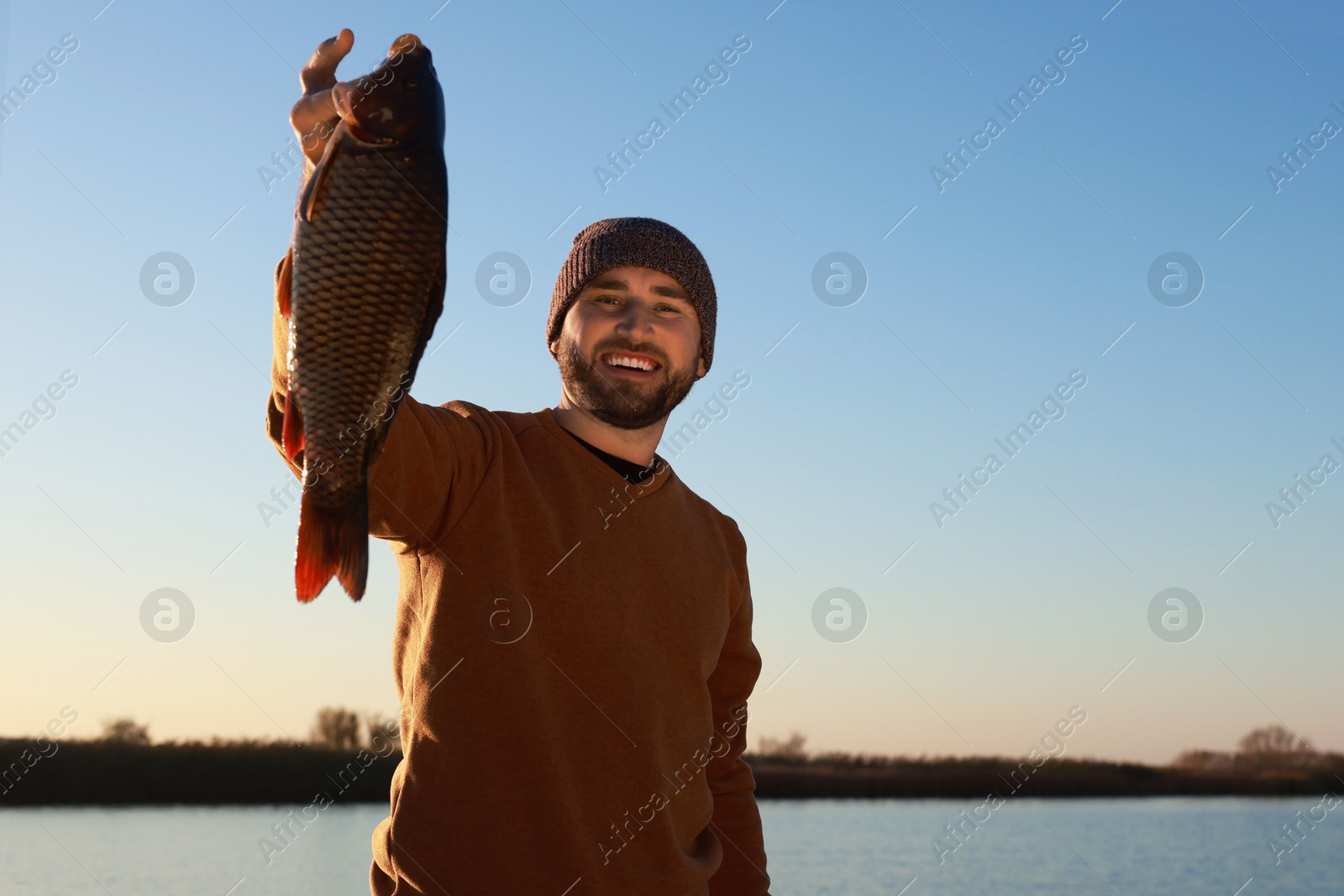 Photo of Fisherman holding caught fish at riverside. Recreational activity