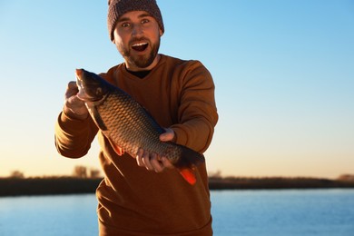 Photo of Fisherman holding caught fish at riverside. Recreational activity