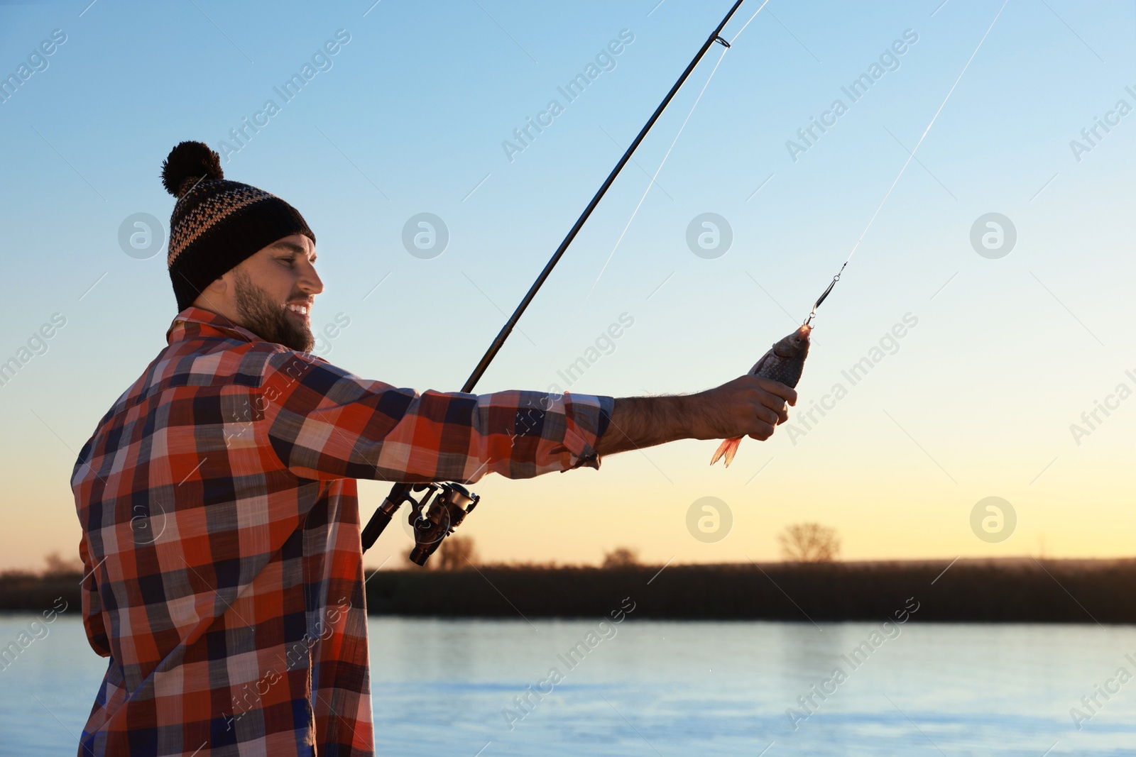 Photo of Fisherman with rod and caught fish at riverside