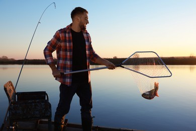 Photo of Fisherman holding fishing net with catch at riverside