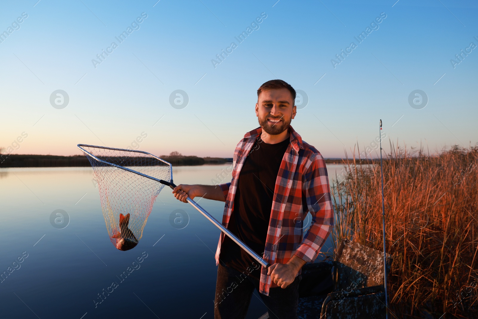 Photo of Fisherman holding fishing net with catch at riverside