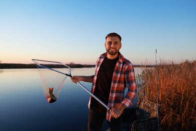 Fisherman holding fishing net with catch at riverside