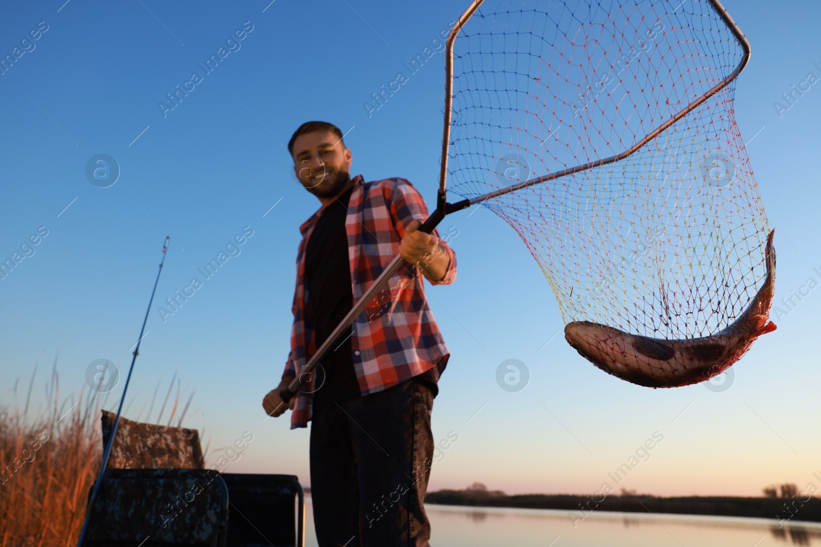 Photo of Fisherman holding fishing net with catch at riverside, low angle view