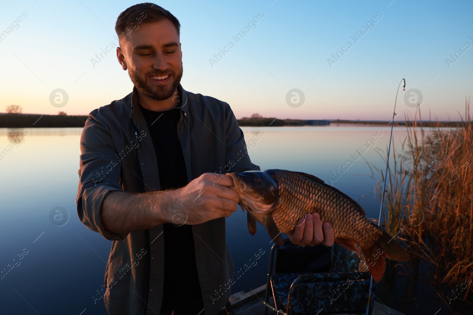 Photo of Fisherman holding caught fish at riverside. Recreational activity