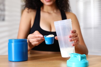 Photo of Beautiful woman making protein shake at wooden table indoors, closeup