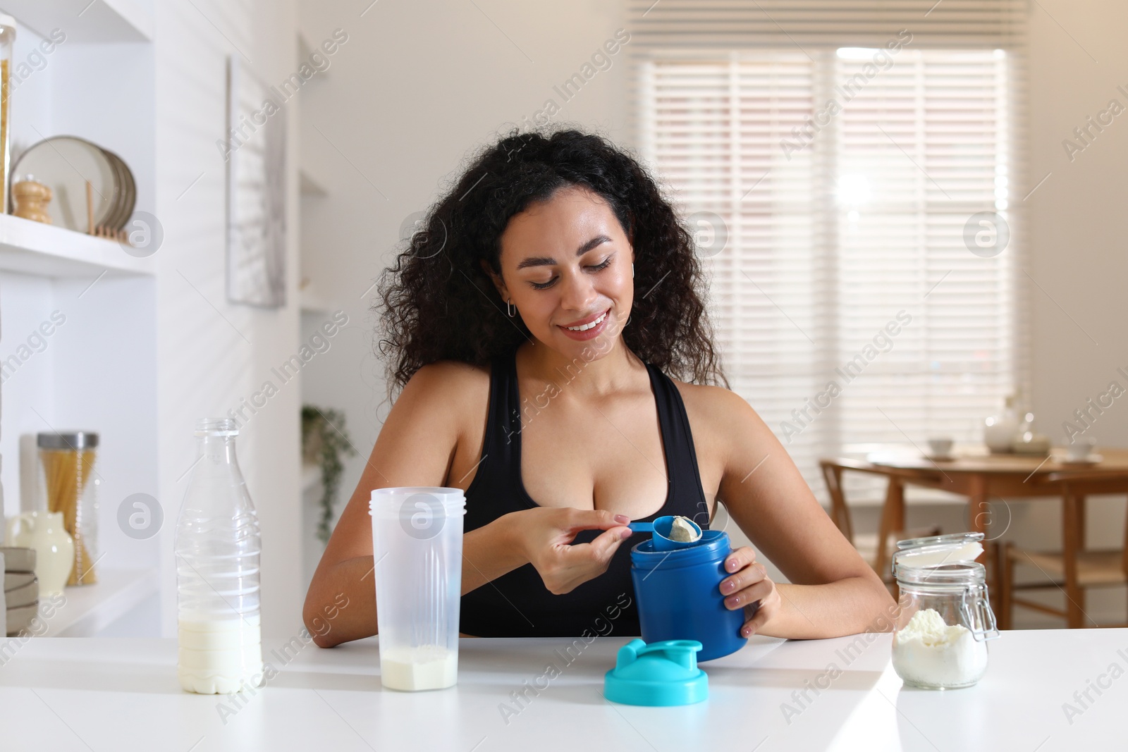 Photo of Beautiful woman making protein shake at white table indoors