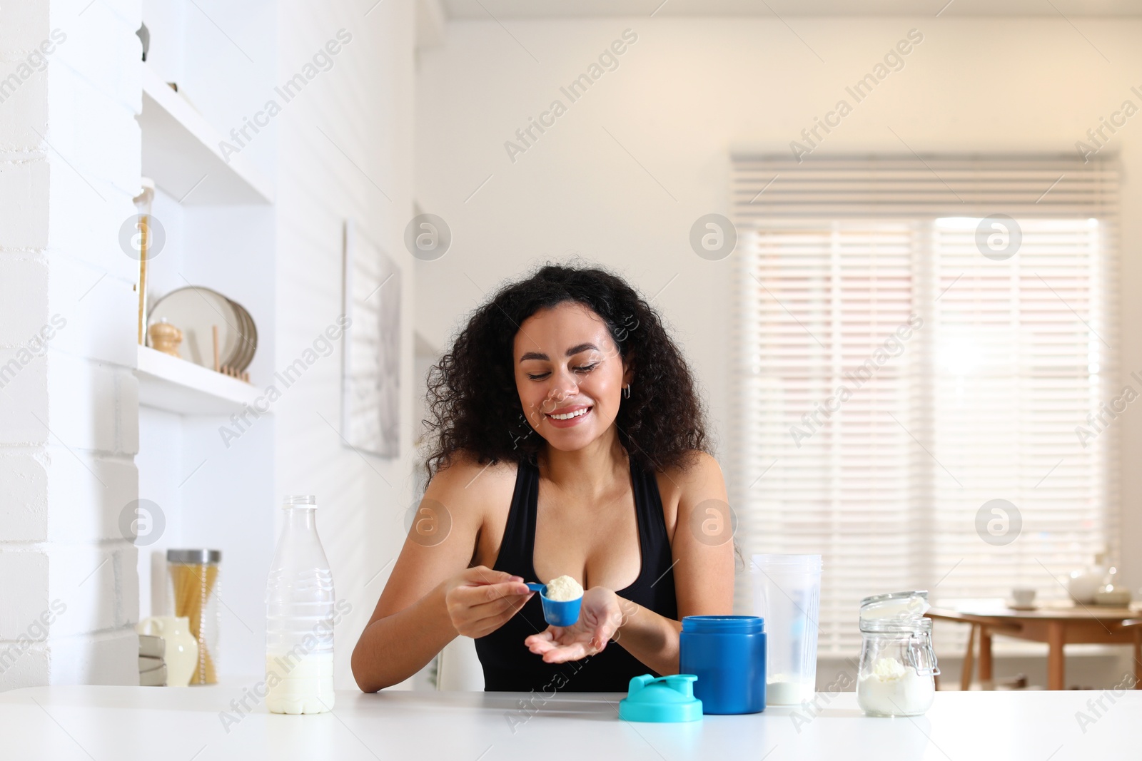 Photo of Beautiful woman making protein shake at white table indoors