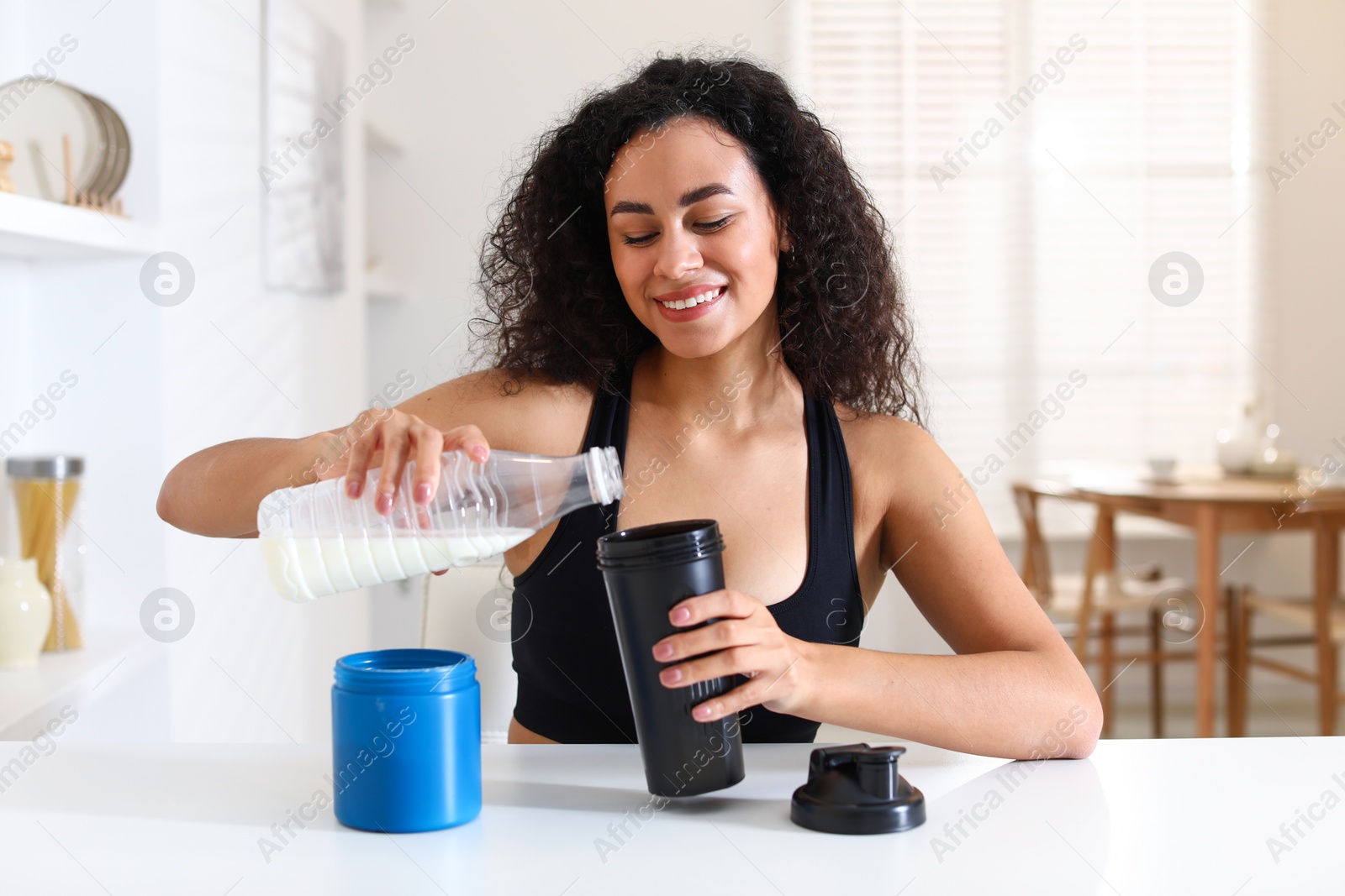 Photo of Beautiful woman making protein shake at white table indoors