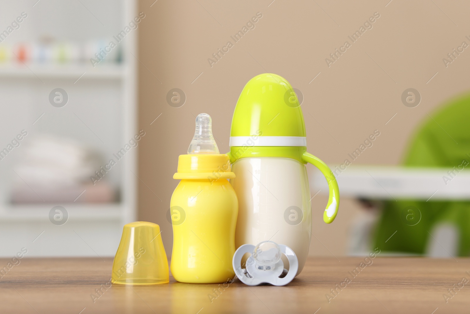 Photo of Feeding bottles with milk and pacifier on wooden table indoors