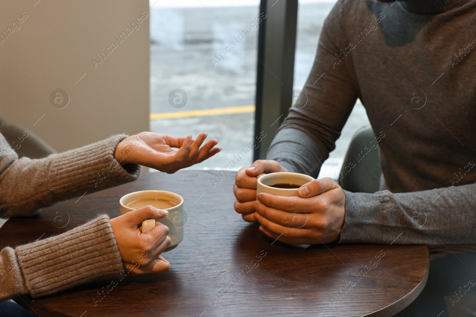 Photo of Colleagues talking during coffee break at wooden table in cafe, closeup