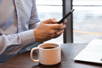 Photo of Businessman with smartphone having coffee break at wooden table in cafe, closeup