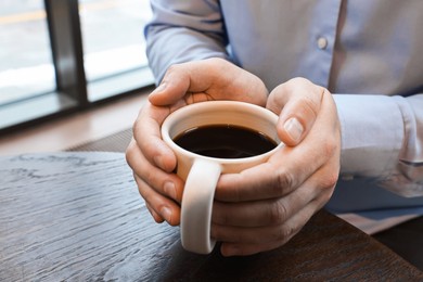 Photo of Businessman having coffee break at wooden table in cafe, closeup