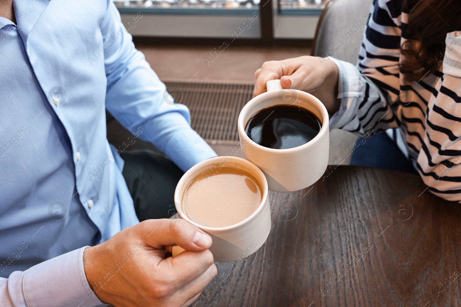 Photo of Colleagues having coffee break at wooden table in cafe, closeup