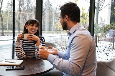 Photo of Happy colleagues talking during coffee break at wooden table in cafe