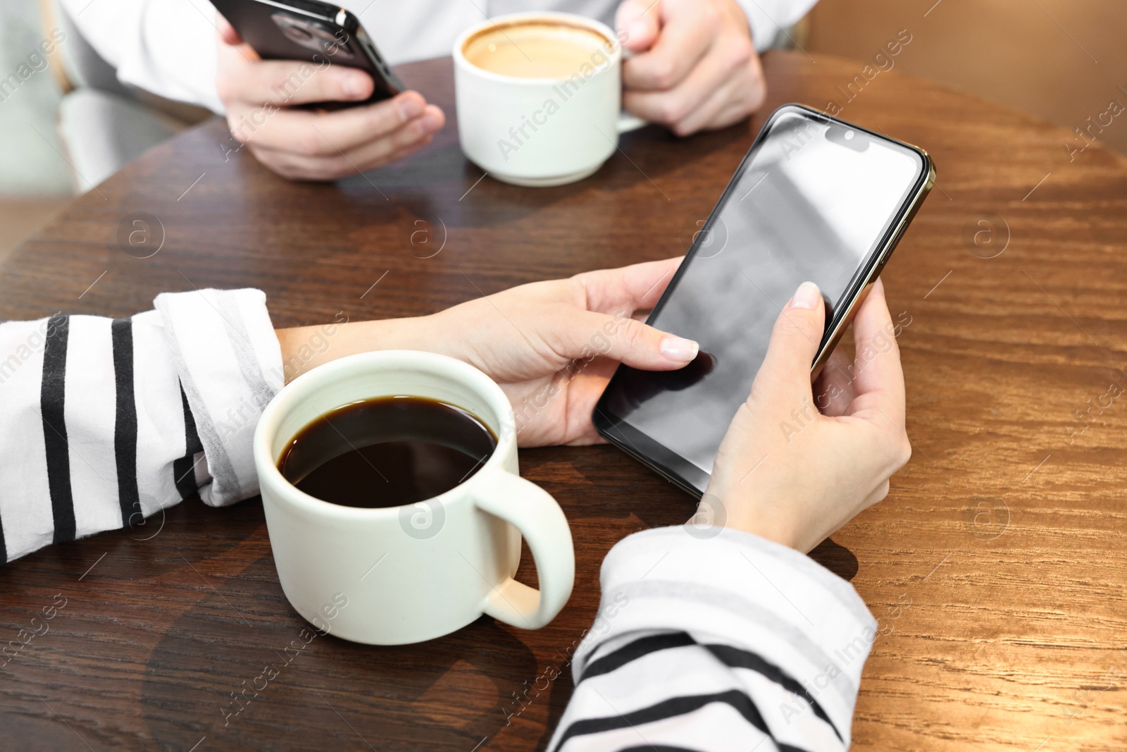 Photo of Colleagues with smartphones having coffee break at wooden table, closeup