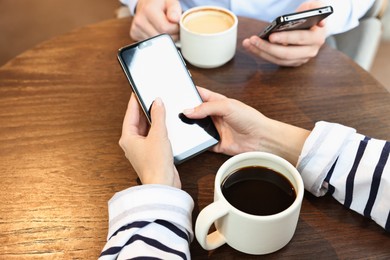 Photo of Colleagues with smartphones having coffee break at wooden table, closeup